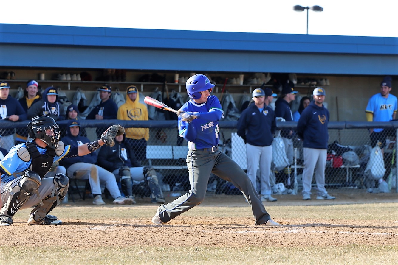 Lucas Weinert just beginning his swing, Rock Valley dugout in the background looking on