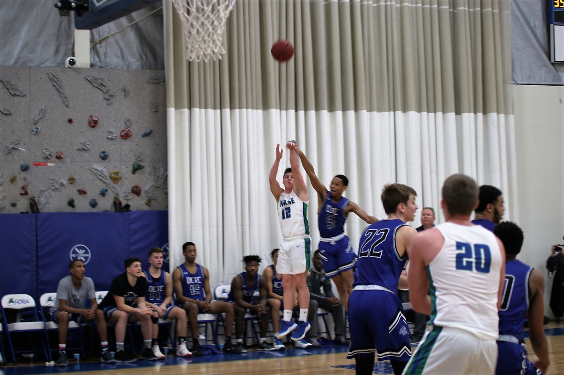 Ryan Arnt after shooting a shot from the sideline in front of the opponent's bench.  The ball is in the air and a defender has attempted to disrupt the shot from behind