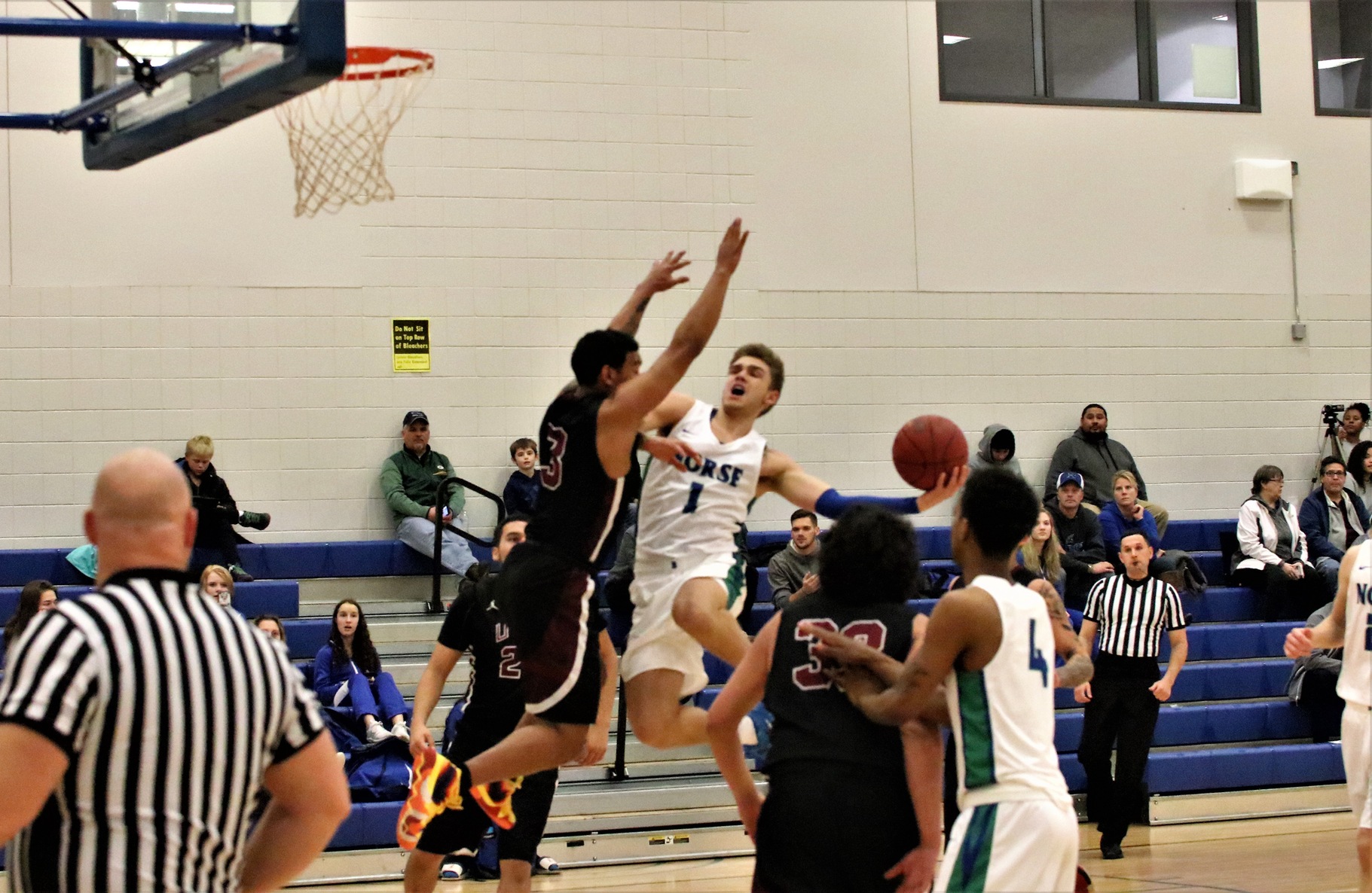 Ryan Robinette in mid air in the middle of the lane, the ball held extended behind him, while a defender is in the air in front of him with his arms up