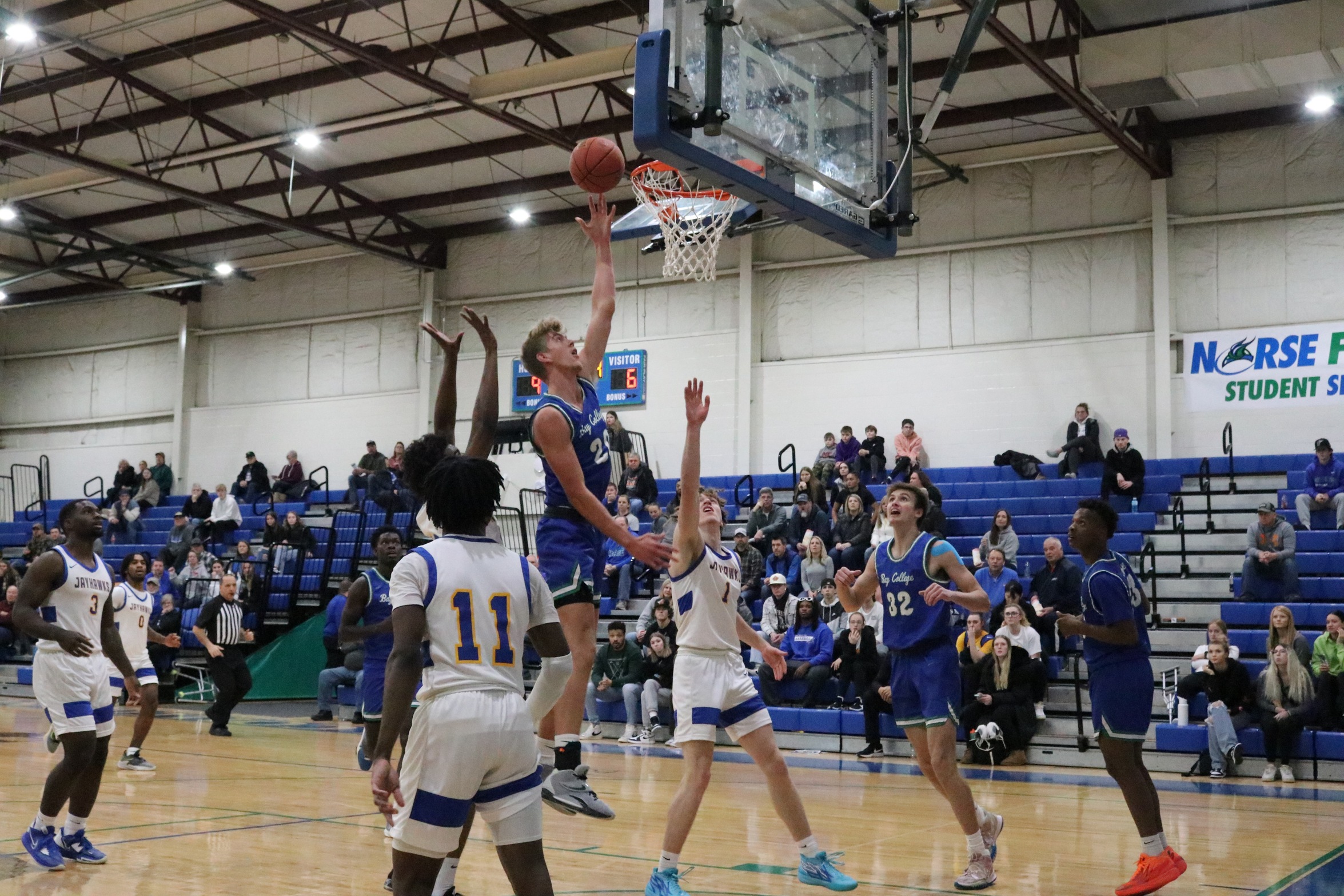 Colin Hudson releasing a shot right at the rim as several players look on