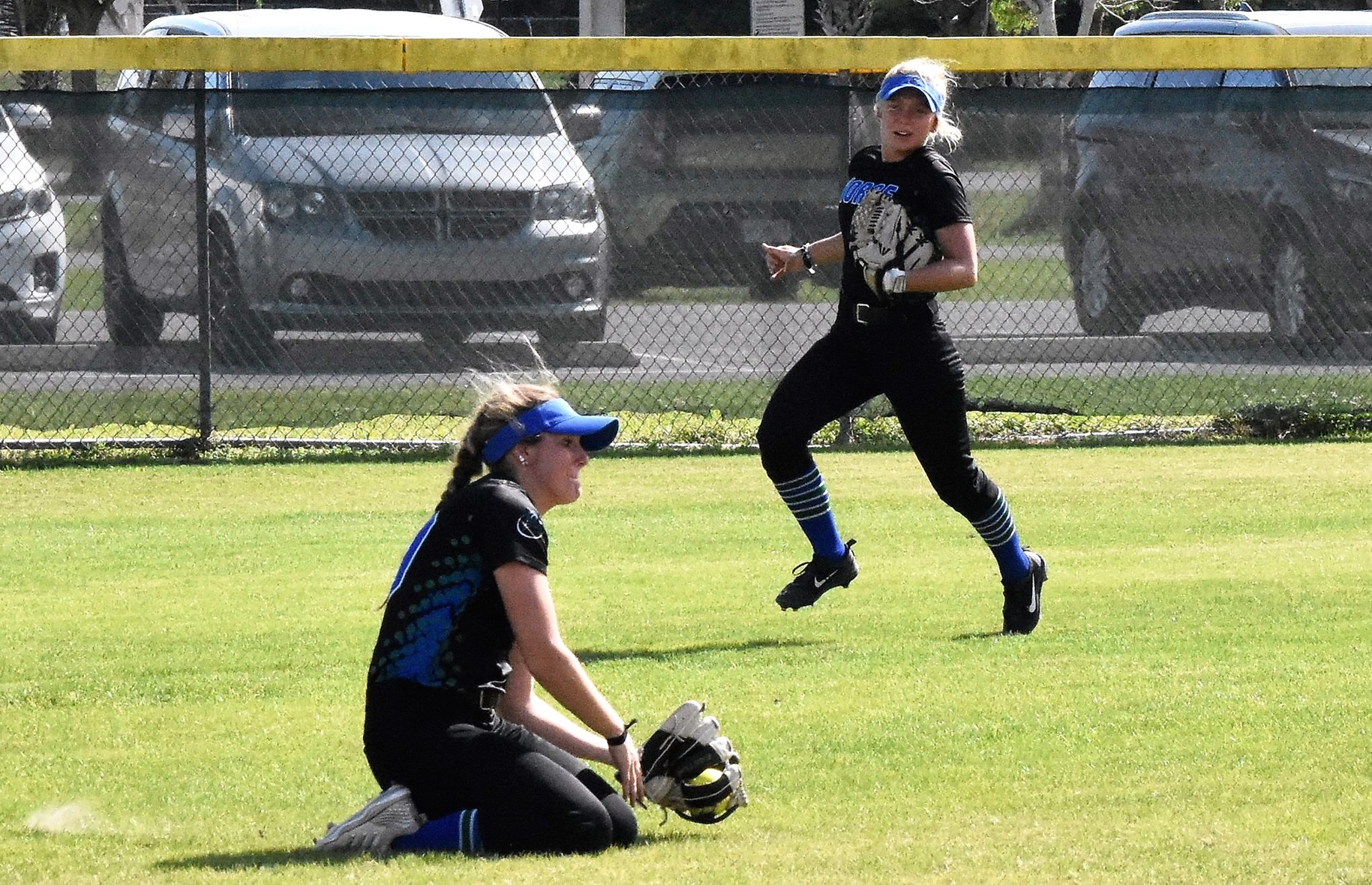 Jerricka McAlpine sliding on her knees and making a catch in the outfield as Emily Bruntjens watches in the background