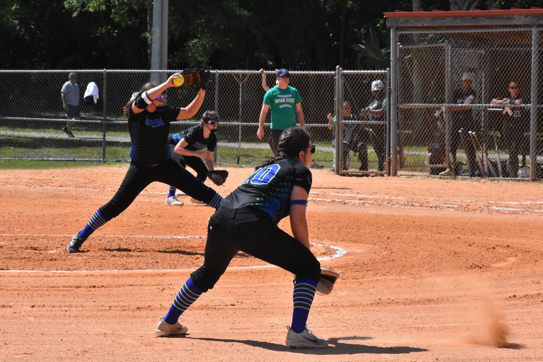 Lexi Winling about to release a pitch while Maddy Griffin gets in her ready position to field in the foreground.
