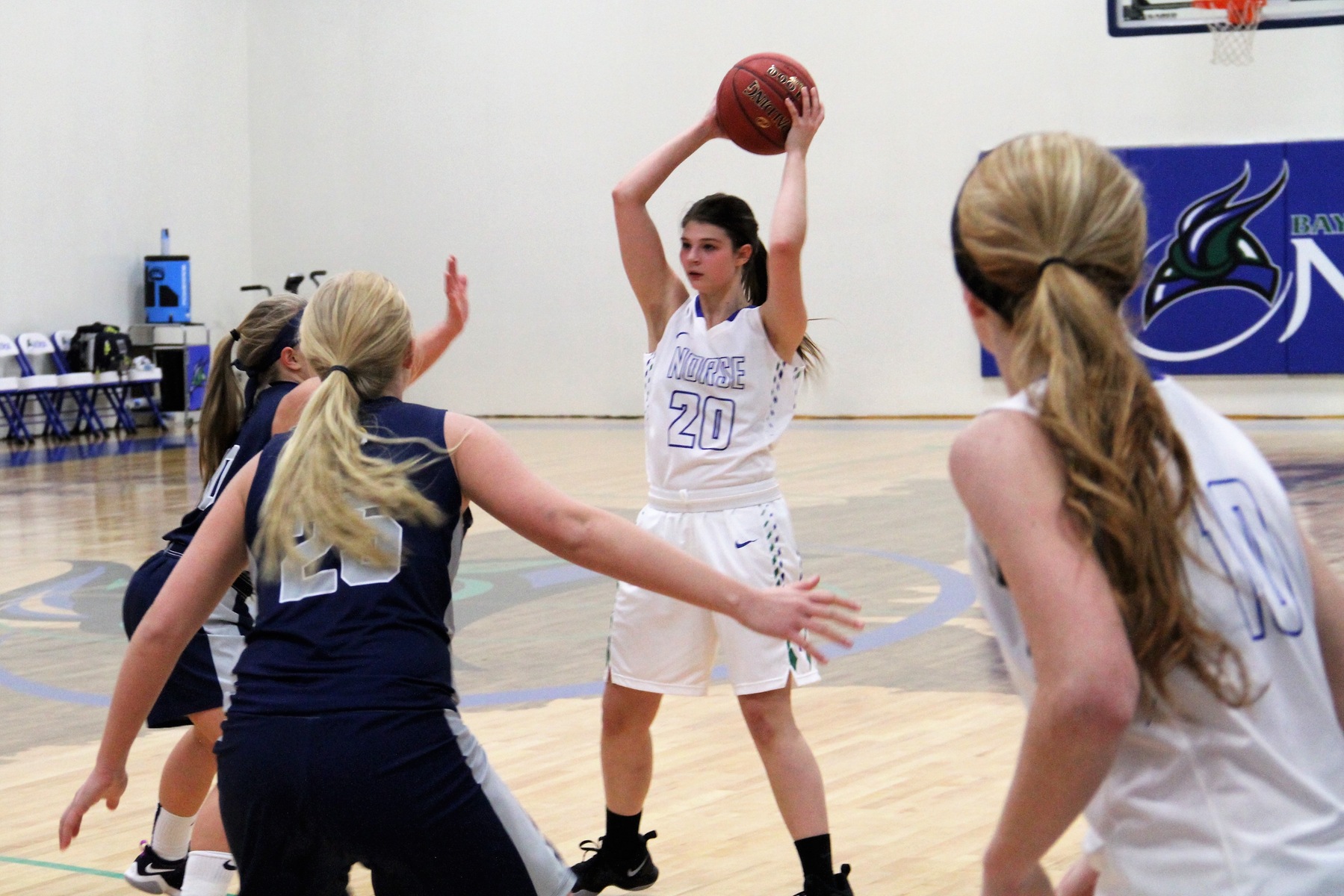 Justice Kinunen holds the ball above her head with a defender close by, Paige Welch and another defender looks on in the foreground